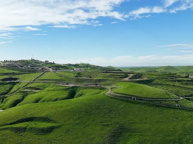 Landscape image of a green hilly field and blue sky