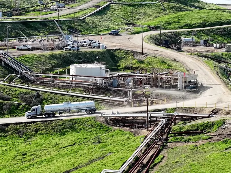 Gazelle worksite with pipelines, storage tanks, and a tanker truck on a dirt road