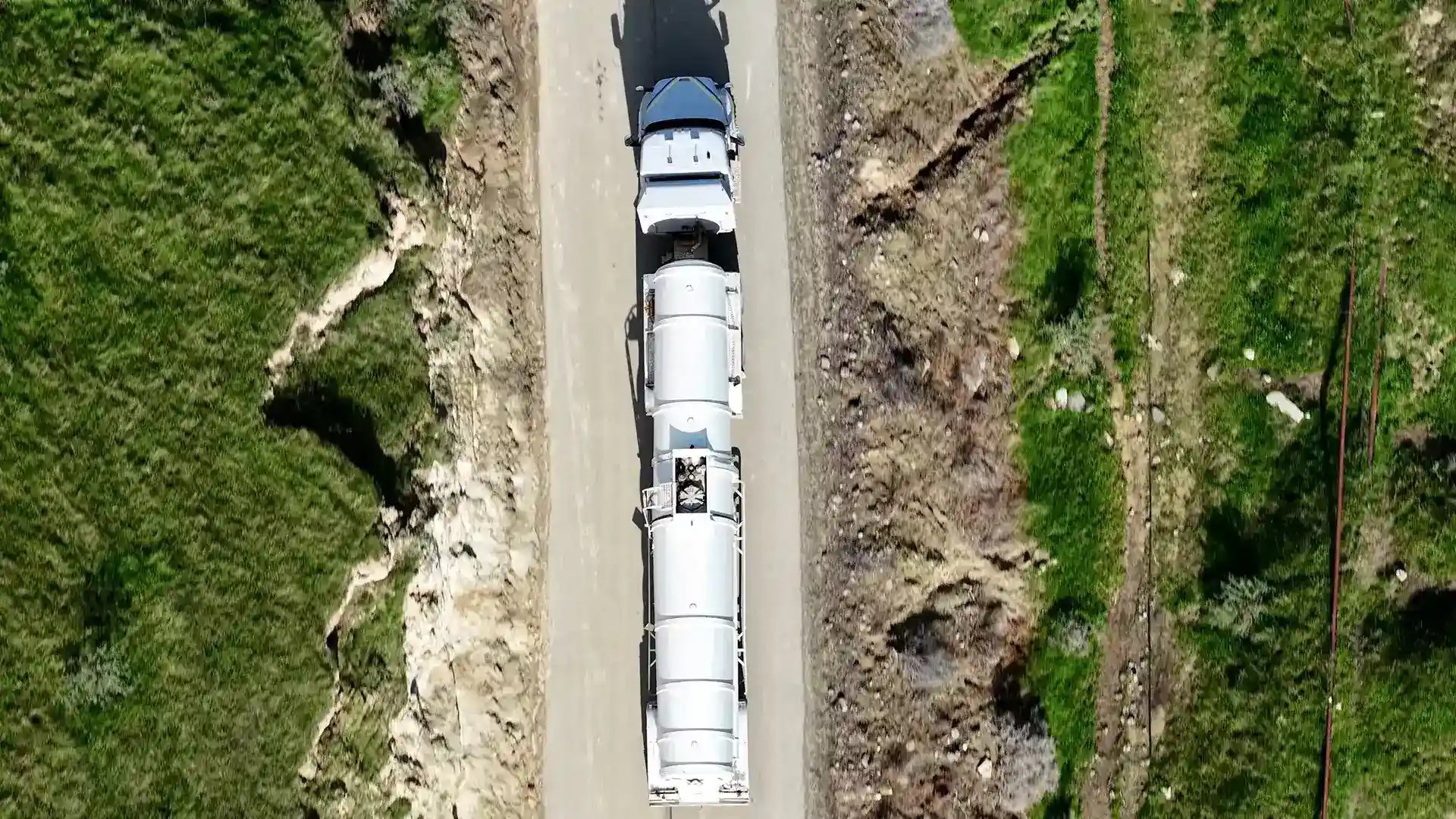 Gallery Tanker truck on a rocky road with green hills on the sides.