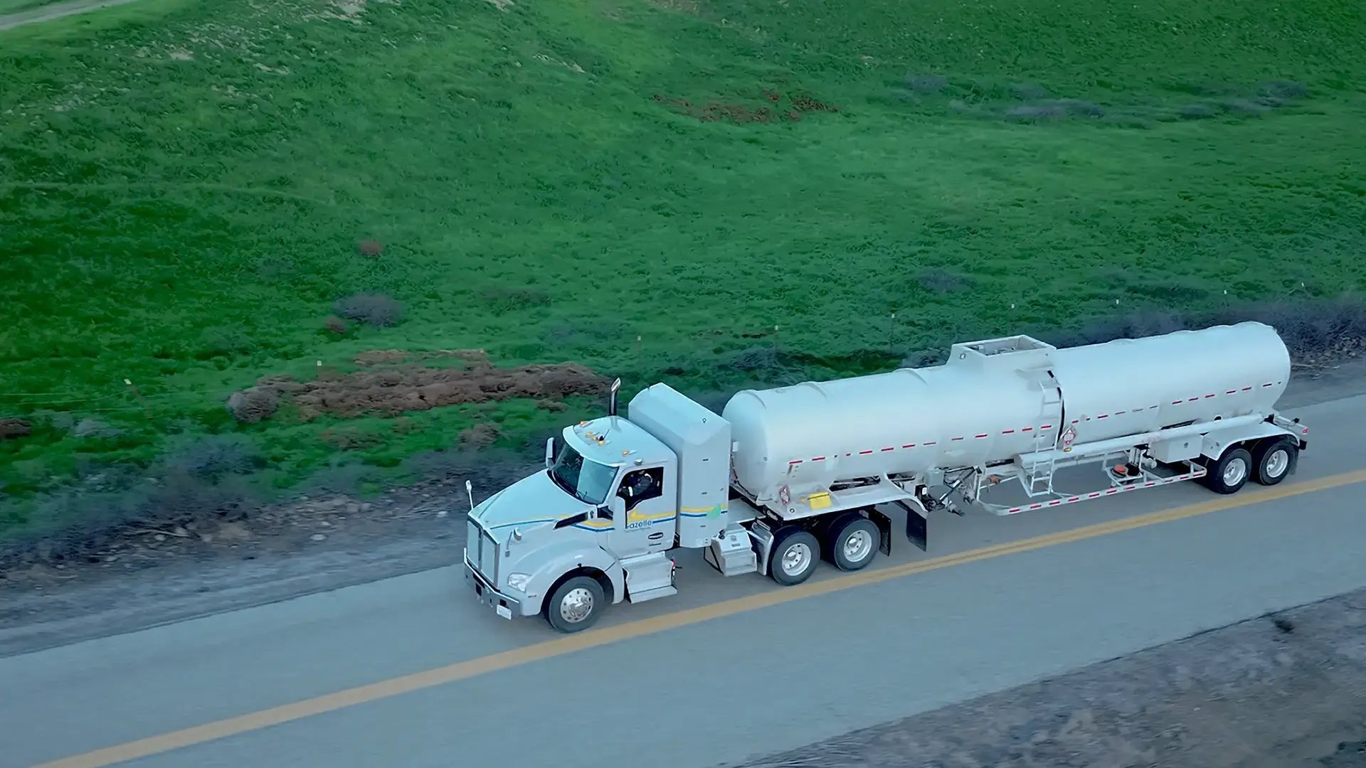 Tanker truck on the road in a grassy hillside.